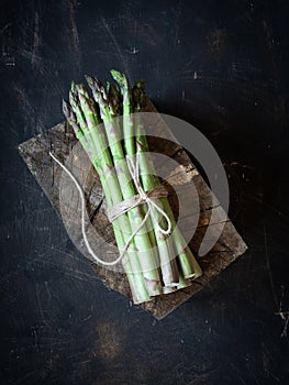 Fresh green asparagus tied by cord on old wood and black background.