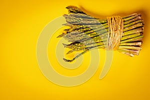 Fresh green asparagus tied with a string on a yellow background