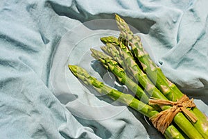 Fresh green asparagus vegetables bunch on blue crumpled fabric background. Healthy diet food