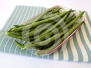 fresh green beans on a rectangular plate with a blue cloth underneath