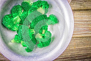 Fresh green broccoli in old metal bowl over rustic wooden desk on wooden background - healthy or vegetarian food concept Top view