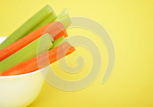 Fresh green celery and carrots on yellow background