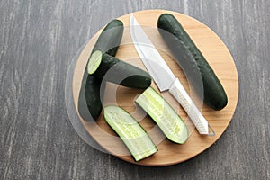 Fresh, green cucumbers on a chopping board with knife are prepared for a nutritious salad or juice on a kitchen table