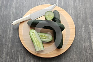 Fresh, green cucumbers on a chopping board with knife are prepared for a nutritious salad or juice on a kitchen table