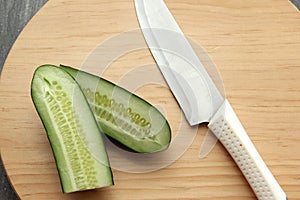 Fresh, green cucumbers on a chopping board with knife are prepared for a nutritious salad or juice on a kitchen table