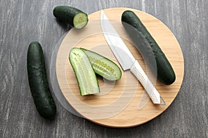 Fresh, green cucumbers on a chopping board with knife are prepared for a nutritious salad or juice on a kitchen table