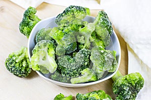 Fresh green frozen broccoli in small white bowl on light background.