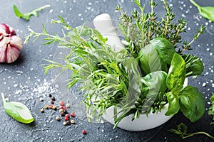 Fresh green garden herbs in mortar bowl and spices on black stone table. Thyme, rosemary, basil, and tarragon for cooking.