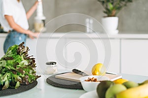 Fresh green healthy fruits and vegetables on table while woman cooking smoothie in kitchen at home