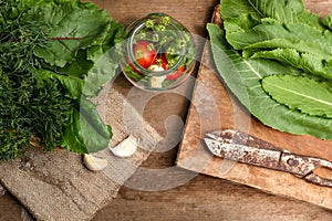 Fresh green herbs, jar with tomatoes, garlic and scissors on wooden table, flat lay