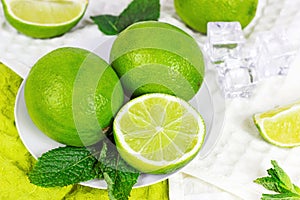 Fresh green juicy limes and lime slices with mint leaves in the kitchen on light background.