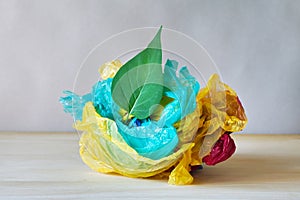 Green leaf and used crumpled colorful plastic bags and wraps on wooden table