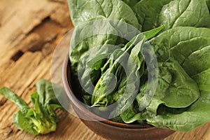 Fresh green leaves of spinach in a bowl on old wooden background