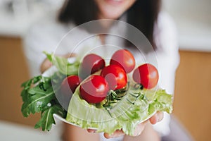 Fresh green lettuce, cherry tomatoes, arugula on plate in woman hands. Healthy eating and diet
