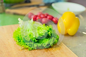 Fresh green lettuce leaves lie on a wooden cutting board next to the yellow bell pepper and red cherry tomatoes on a