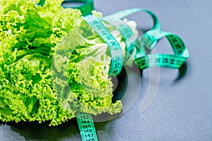 Fresh green lettuce salad leaves with measuring tape on dark background. The concept of a healthy lifestyle, diet, healthy food.