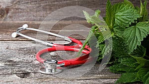 Fresh green nettle leaves and stethoscope on wooden background