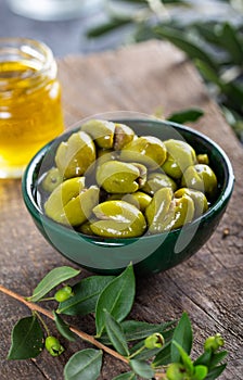 Fresh green olives in a green ceramic bowl. Olive oil and olive tree leaves in a glass jar in the background