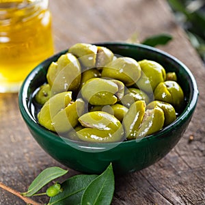 Fresh green olives in a green ceramic bowl. Olive oil and olive tree leaves in a glass jar in the background