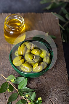 Fresh green olives in a green ceramic bowl. Olive oil and olive tree leaves in a glass jar in the background