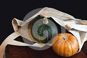 Fresh green and orange pumpkins in bag on wooden table