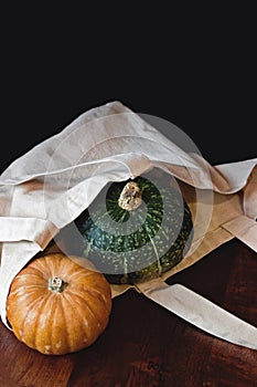 Fresh green and orange pumpkins in bag on wooden table