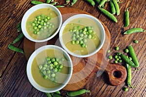 Fresh green pea soup with pea seeds and pea pods around . Selective Focus, Focus on the pea in the middle of the soup