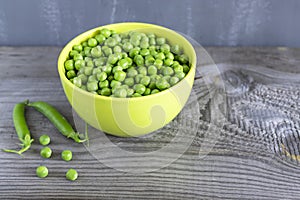 Fresh green peas in green cup on wooden background. Rustic table background
