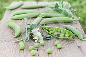 Fresh green peas, pods and flowers on wooden surface