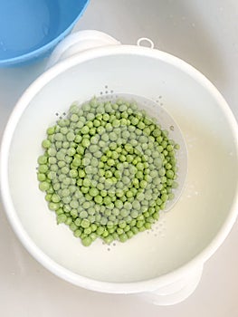 Fresh green pease in a white colander