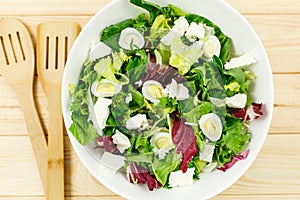 Fresh green salad with goat cheese, eggs in big white bowl on wooden table. Vegan salad with green mix leaves and vegetables
