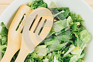 Fresh green salad with goat cheese, eggs in big white bowl on wooden table. Vegan salad with green mix leaves and vegetables