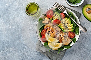 Fresh green salad with grilled chicken fillet, spinach, tomatoes, avocado, lemon and black sesame seeds with olive oil in white bo