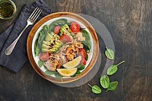 Fresh green salad with grilled chicken fillet, spinach, tomatoes, avocado, lemon and black sesame seeds in white bowl on old woode