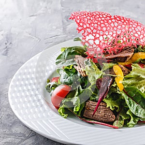 Fresh green salad with lettuce, arugula, sweet pepper, tomatoes and beef in plate over dark table. Healthy food