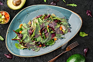 Fresh green salad with mixed greens, spinach arugula, pumpkin, avocado in plate over dark background.