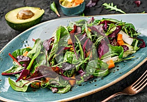 Fresh green salad with mixed greens, spinach arugula, pumpkin, avocado in plate over dark background.