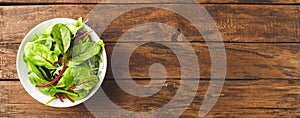 Fresh green salad with spinach, arugula and beetroot leaves in bowl on vintage wooden background with copyspace. Top view.