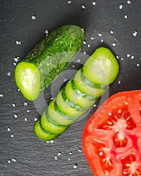 Fresh green sliced cucumber and tomato on a black stone background.