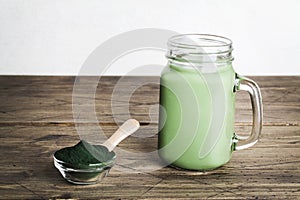 fresh green smoothie in glass bottle and spirulina powder with spoon on wooden background. useful habits