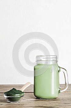 fresh green smoothie in glass bottle and spirulina powder with spoon on wooden background. useful habits