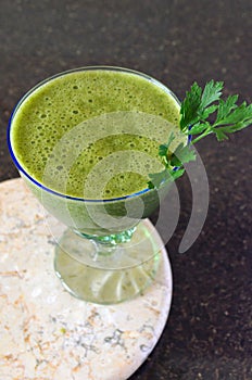 Fresh green smoothie in a wide glass on stem on the kitchen countertop - close up front top view