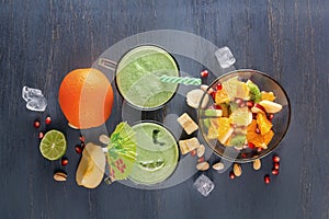 Fresh green smoothies in a glass mug fruits, vegetables and fruit salad on a wooden table with ice