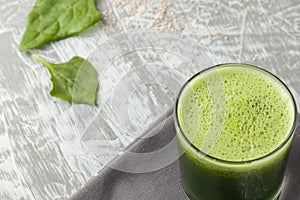 Fresh green spinach smoothie in a glass cup on a gray wooden surface. Flat layout