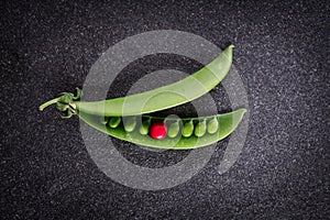 Fresh green sweet peas with differnt one red seed on black ston