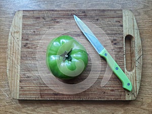 a fresh green tomato with a knife on a cutting board