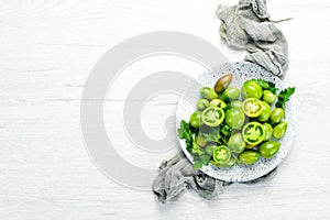 Fresh green tomatoes in a plate on a white wooden background. Greens. Top view.