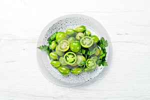Fresh green tomatoes in a plate on a white wooden background. Greens. Top view.