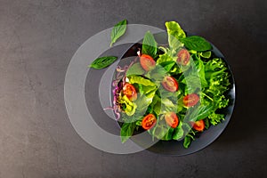 Fresh green vegetable salad. Top view from above of cherry tomato, basil, spinach and lettuce, red cabbage in black bowl.