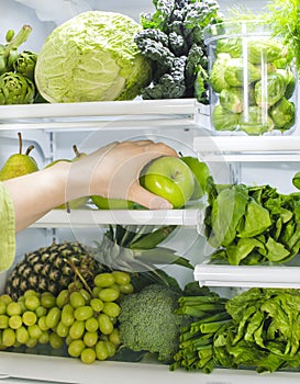 Fresh green vegetables and fruits in fridge. Woman takes the green apple from the open refrigerator.